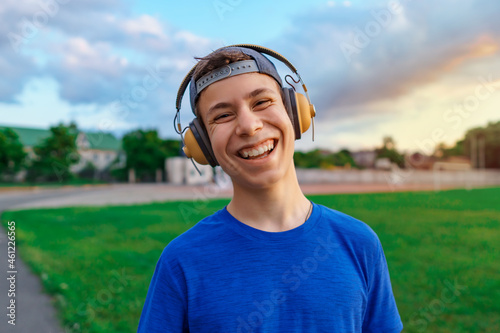 happy teen boy portrait at a sport stadium, he's wearing headphones and smiling, a soccer field with green grass - sports and health concept