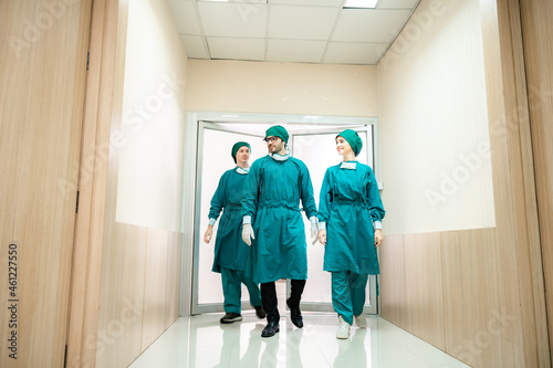 Group of young male and female doctors in surgery uniform speaking to each other congratulating for successful operation while walking in hospital hallway © chokniti