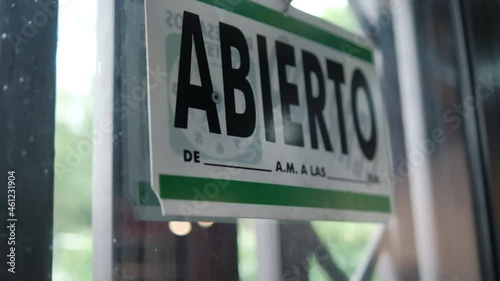 Green and white sign with the word open in Spanish on window