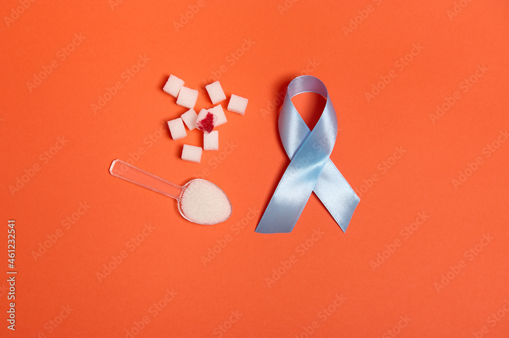 Pure refined white sugar cubes with blood drop and blue satin ribbon, symbol of World diabetes awareness day 14 November. Isolated over colored orange background, copy space for medical ad. Flat lay Pure refined white sugar cubes with blood drop and blue satin ribbon, symbol of World diabetes awareness day 14 November. Isolated over colored orange background, copy space for medical ad. Flat lay
