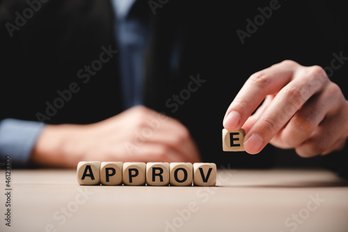 Closeup of wooden cubes with letters and word approve on table with unrecognized man in formal clothing of suit and tie sitting with hands placed on desk during a job interview