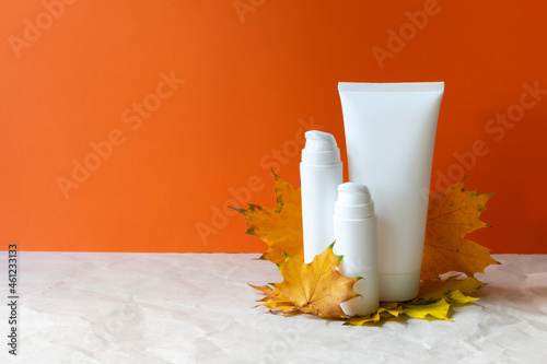 Autumn skin care cosmetic bottles cream yellow fall leaves maple on orange background copy space
