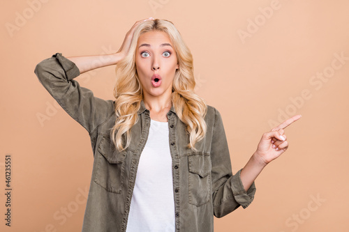 Photo of young girl amazed shocked hand touch head point finger empty space advertise isolated over beige color background photo