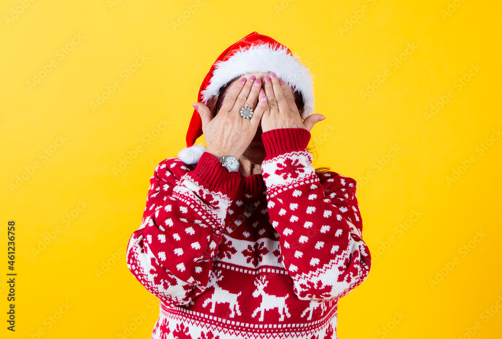 senior woman covers her face with her hands, wearing santa calus hat senior woman covers her face with her hands, wearing santa calus hat