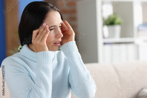 Woman with headache and photophobia looks out window photo