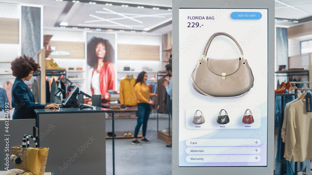 Shot of a Floor-Standing LCD Touch Screen Display with User Interface of Online Clothing Shop Standing in Clothing Store. Self service Checkout. Diverse People in Fashionable Shop Buying Clothes. - obrazy, fototapety, plakaty 
