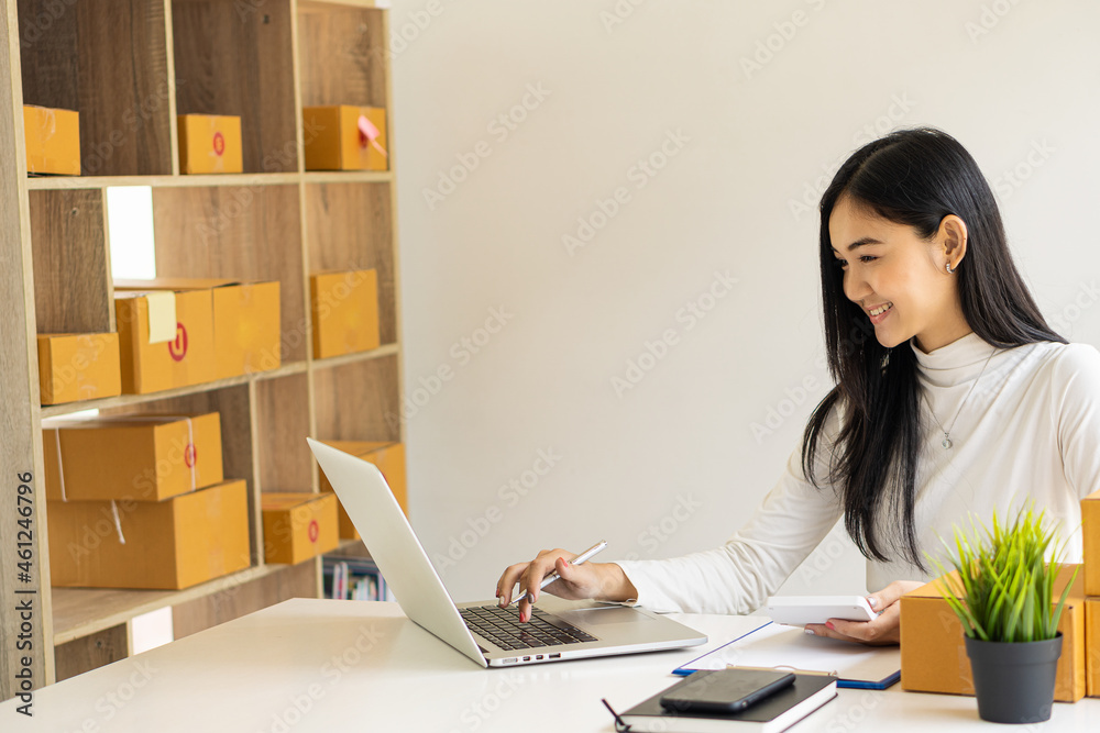 Asian girl startup Small sme business owners work with laptop computers and smartphones at work. with parcel paper boxes for delivery to customers online selling, eCommerce, packing ideas, work from h Asian girl startup Small sme business owners work with laptop computers and smartphones at work. with parcel paper boxes for delivery to customers online selling, eCommerce, packing ideas, work from h