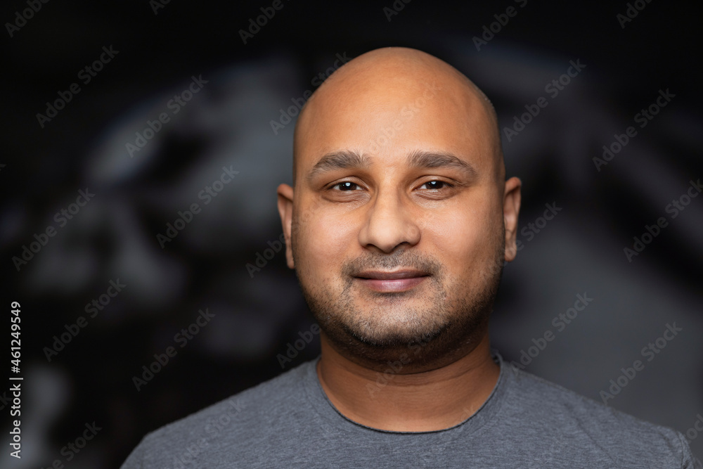 Obraz premium Portrait of a bald man smiling against dark backdrop.