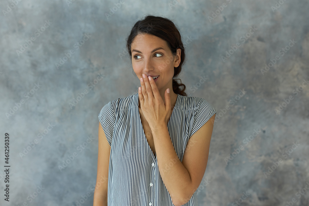 Good-looking, lovely young brunette girl posing against grey textured studio wall with oops gesture, having joyful look, smiling widely, looking aside, wearing striped shirt-sleeved blouse Good-looking, lovely young brunette girl posing against grey textured studio wall with oops gesture, having joyful look, smiling widely, looking aside, wearing striped shirt-sleeved blouse