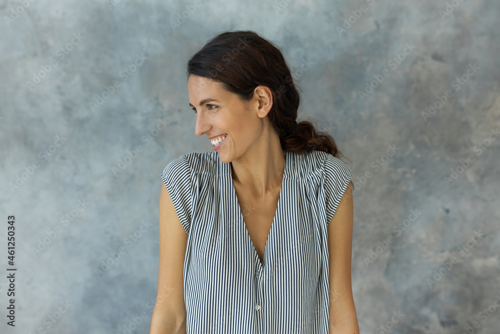 Positive young attractive Caucasian brunette woman standing in front of camera with head turned to right side, laughing, keeping hands down straight, dressed in casual shirt-sleeved lovely dress Positive young attractive Caucasian brunette woman standing in front of camera with head turned to right side, laughing, keeping hands down straight, dressed in casual shirt-sleeved lovely dress