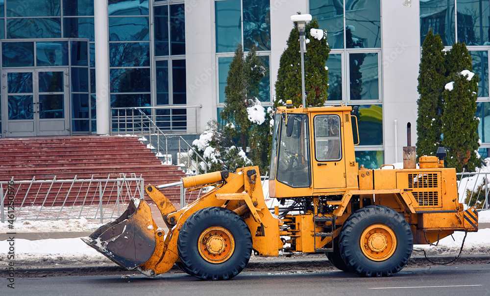 Yellow front loader with scoop for clearing snow. Wheel loader machine ready to removing snow in winter. Municipal service vehicle parked at street. Municipal city service cleans street from snow