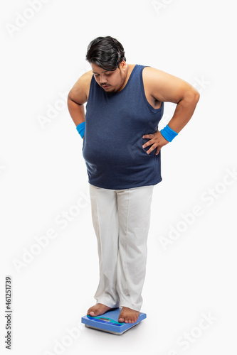 Fototapeta Portrait of a fat man standing on weighing machine and measuring weight