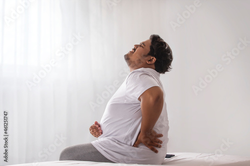  A fat man sitting and holding his belly and back in pain.