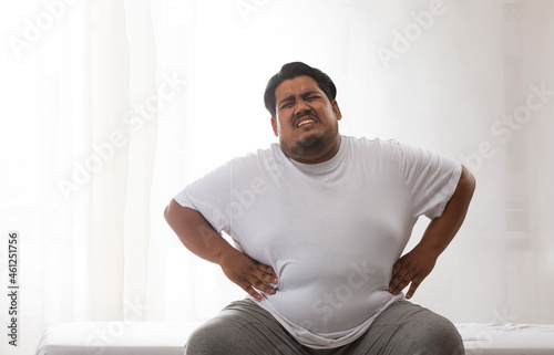 Fotografie A fat man sitting and holding his belly in pain.