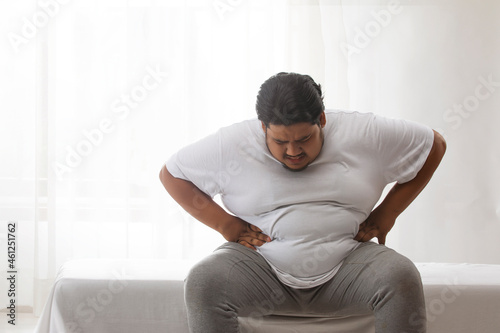  A fat man sitting and holding his belly in pain.