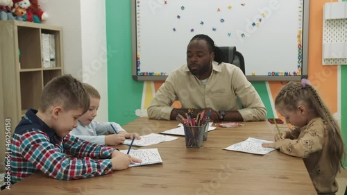 An African American teacher teaches a group of children to draw while sitting at a table in the classroom. School for Children, Teaching Adolescents, Gain Knowledge, Learn the Language.