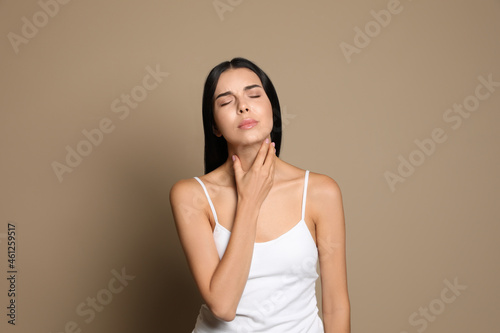 Young woman doing thyroid self examination on beige background