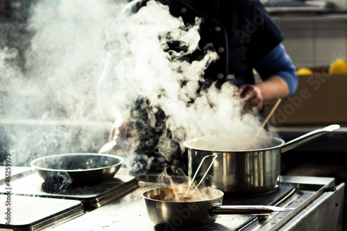 Fotografie Chef cooking soup and water evaporating from a pot at a restaurant kitchen