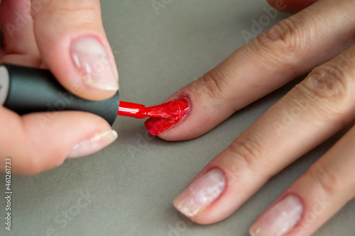 application of red gel polish on the nails of a woman s hand. part of the nails without coating. manicure at home