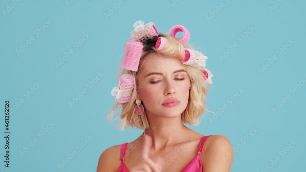 Confident pin-up woman in curlers showing no gesture in blue studio