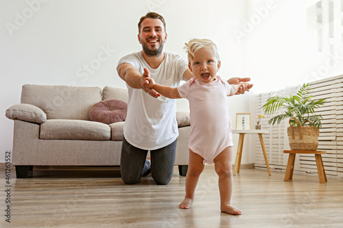 Father and daughter spending quality time together.A child learning to walk. Bearded man with his adorable blonde toddler. Close up, copy space for text, background. photo