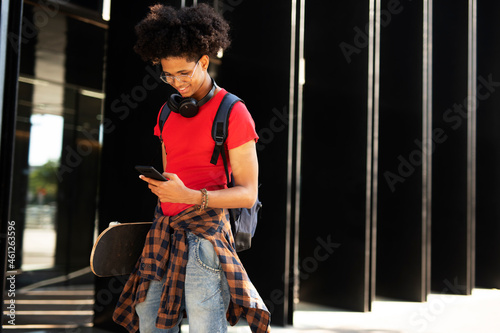 Portrait of happy african-american man with skateboard. Young fashion man with skateboard using the phone
