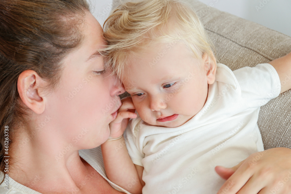 Portrait of a loving young mother kissing her toddler child. Woman with her blonde child having fun at home. Close up, copy space for text, background. Portrait of a loving young mother kissing her toddler child. Woman with her blonde child having fun at home. Close up, copy space for text, background.