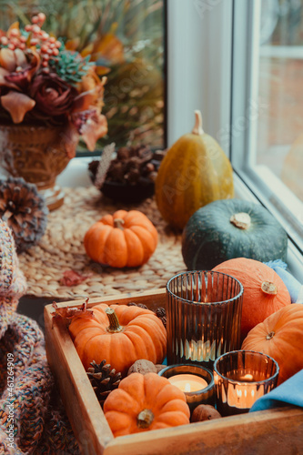 Autumn cozy mood composition on the windowsill. Pumpkins, cones, candles on wooden tray, fflowers and warm plaid. Autumn, fall, hygge home decor. Vertical card. Selective focus. Copy space. photo