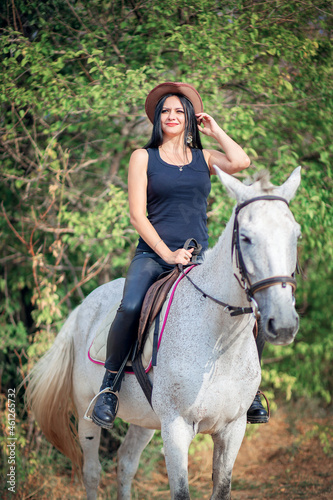 Beautiful woman in cowboy hat and leather pants rides a gray horse © borisenkoket