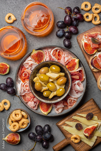 Appetizers with cocktails. Artichoke canned, olives, bruschetta with italian prosciutto cotto, crudo and figs, cheese, grape. Grey stone surface. Vertical image.