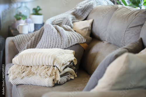 Stack of a variety of soft knit throw blankets stacked on a grey couch in a farmhouse style living room. Selective focus on covers with blurred foreground and background. photo