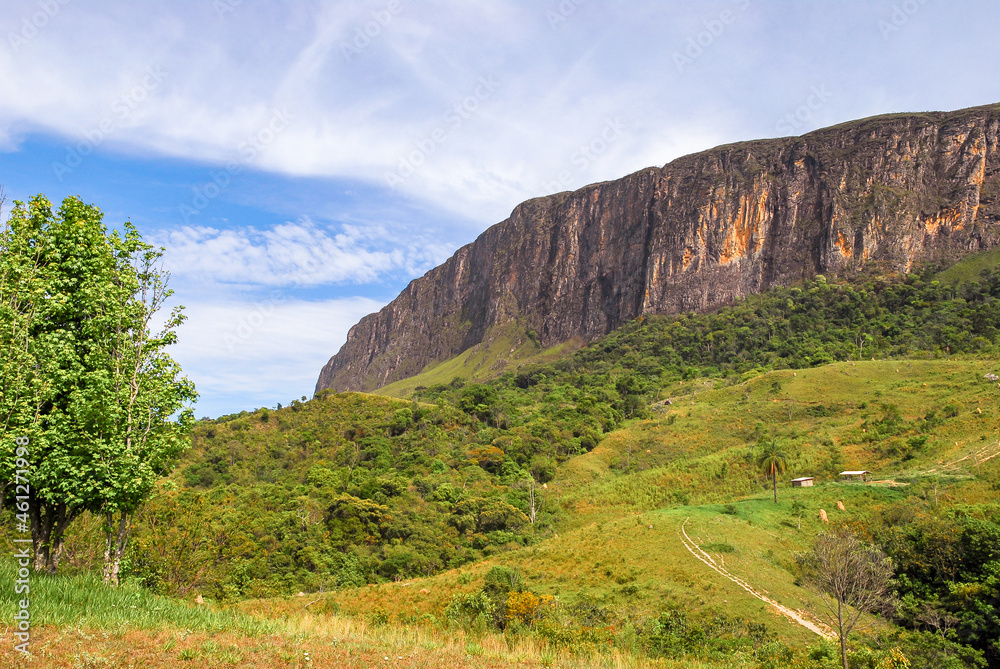 Large rock wall, from the Serra da Canastra park massif, with forest and pastures, sunny day and blue sky with clouds, São Roque de Minas, Minas Gerais, Brazil