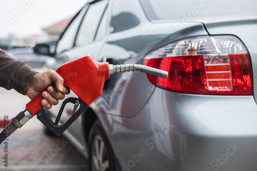 A gas station worker holds a fuel dispenser to fill the car with fuel. A young man's hand holds a gas nozzle to refuel with self-service in a gas station.