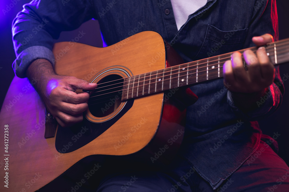 Obraz premium Close up hands young man playing acoustic guitar on stage live in concert. With neon light. Young man practicing music and solo guitar on the show.