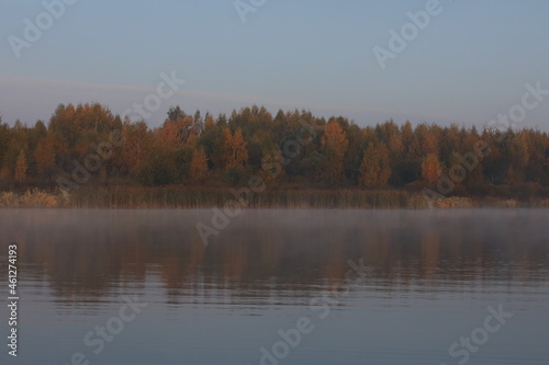 Autumn landscape with beautiful yellow orange forest by the lake in the fog in the early morning