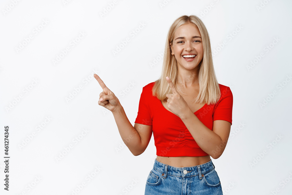 Happy smiling woman pointing fingers at upper left corner, showing advertisement or logo, standing over white background Happy smiling woman pointing fingers at upper left corner, showing advertisement or logo, standing over white background