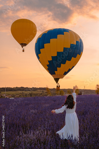woman standing at lavender field looking at air balloons with basket