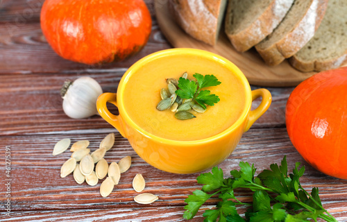 Pumpkin cream soup and freshly baked homemade bread on a wooden background. Close-up.