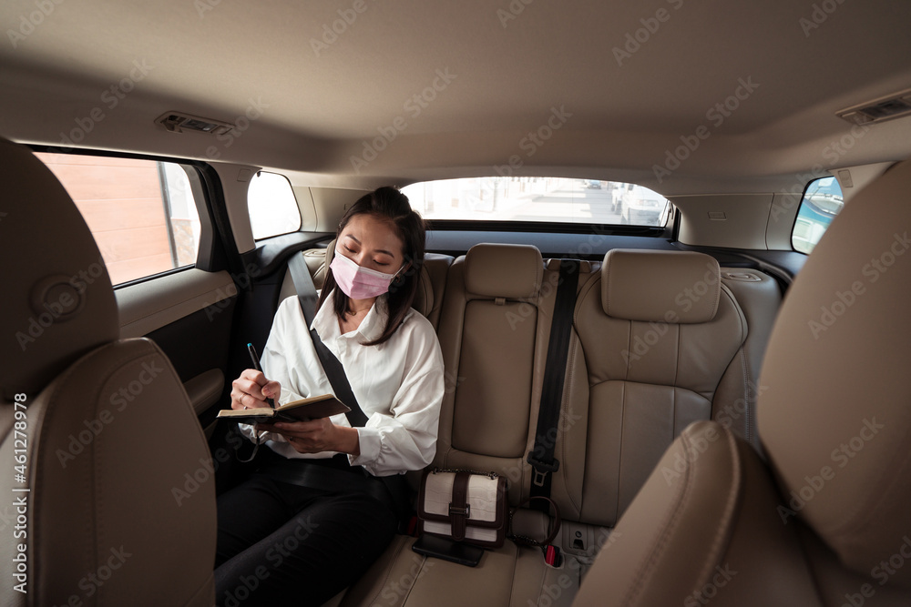 Focused ethnic woman taking notes in notebook in taxi