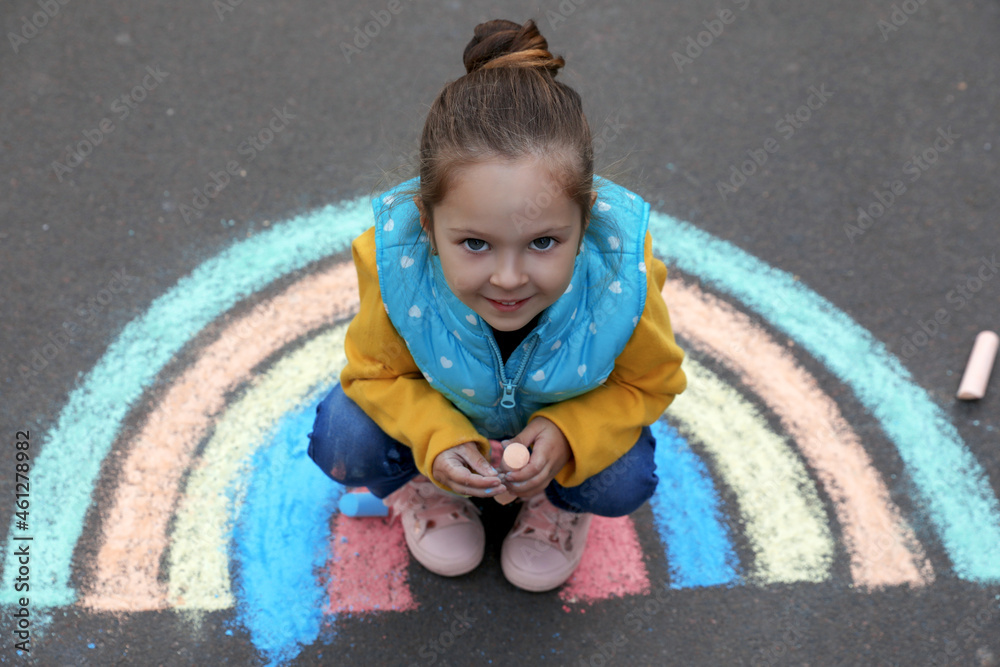 Fototapeta premium Happy child near chalk drawing of rainbow on asphalt, above view
