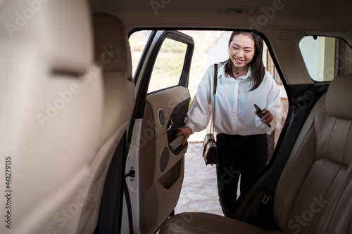 Crop positive ethnic female passenger in formal wear with smartphone opening the back door of the car photo