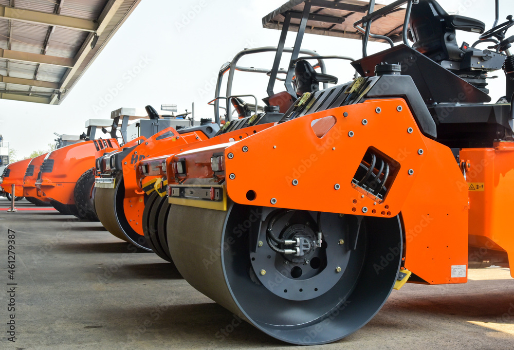An orange road roller is parked in the company. An orange road roller is parked in the company.