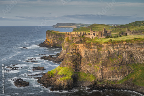 Dunluce Castle illuminated by sunlight, perched on the edge of cliff, Bushmills, Northern Ireland. Filming location of popular TV show Game of Thrones