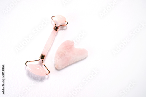 Pink face roller and gua sha massager made from natural quartz stone over white background with drops . Lifting and toning treatment at home.