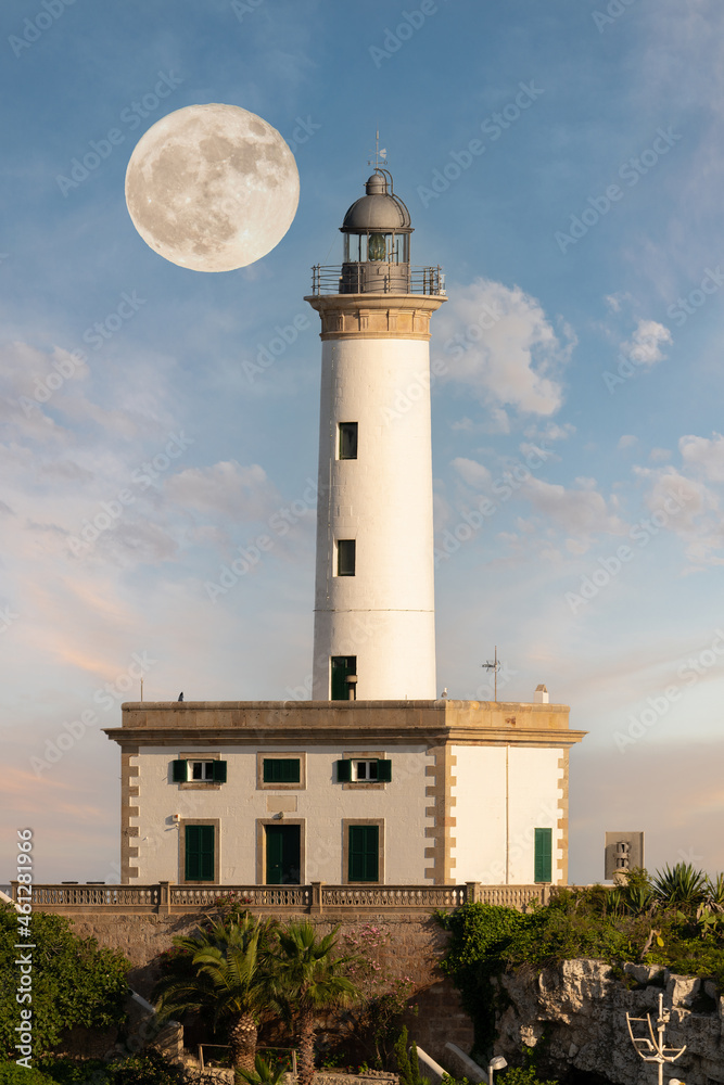 The Ibiza lighthouse at sunset. The full moon is in the sky behind the tower. It's a summer evening with a romantic mood and beautiful clouds.