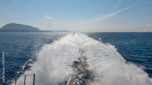 View from the stern of the high-speed ferry to the mountainous Spanish east coast near Denia in Spain. The large and fast catamaran creates a wide and long stern wave. Spray is in the air. © wewi-creative