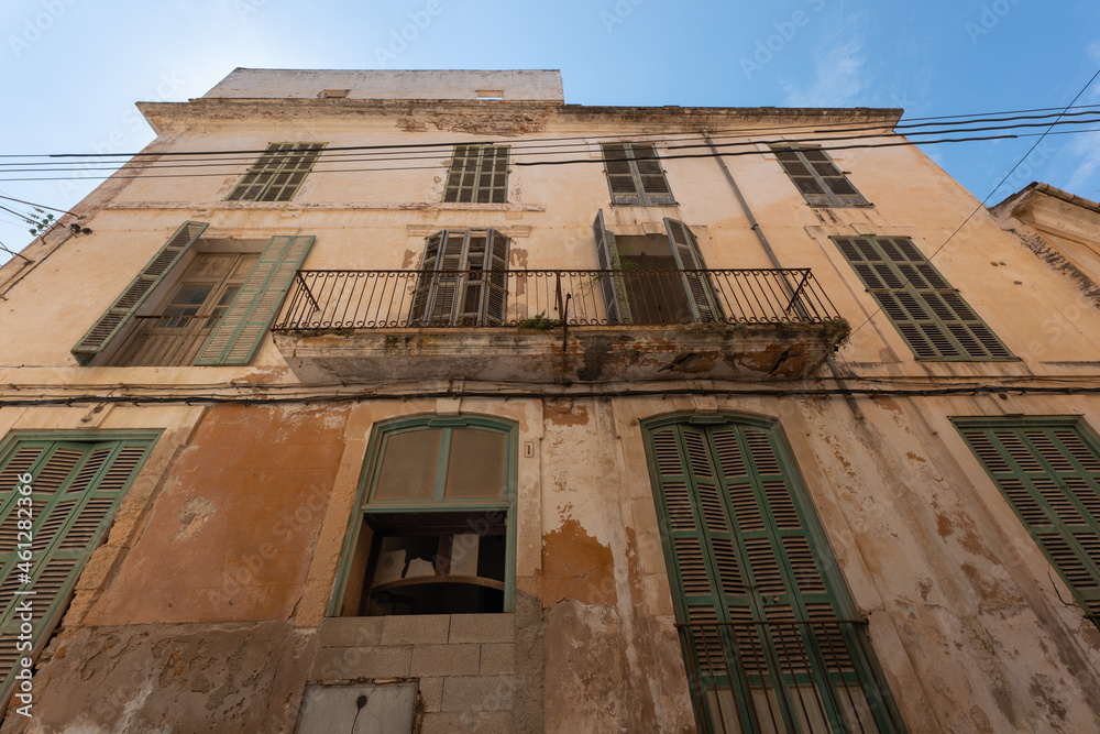 A typical Spanish house facade in the old town of Felanitx on the Spanish island of Mallorca. The windows are closed with wooden shutters. Electric cables hang on the wall.
