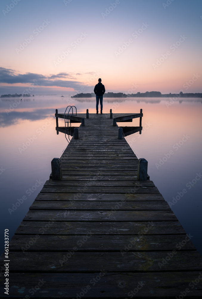 Obraz premium A man looking over a lake during a foggy, tranquil morning.