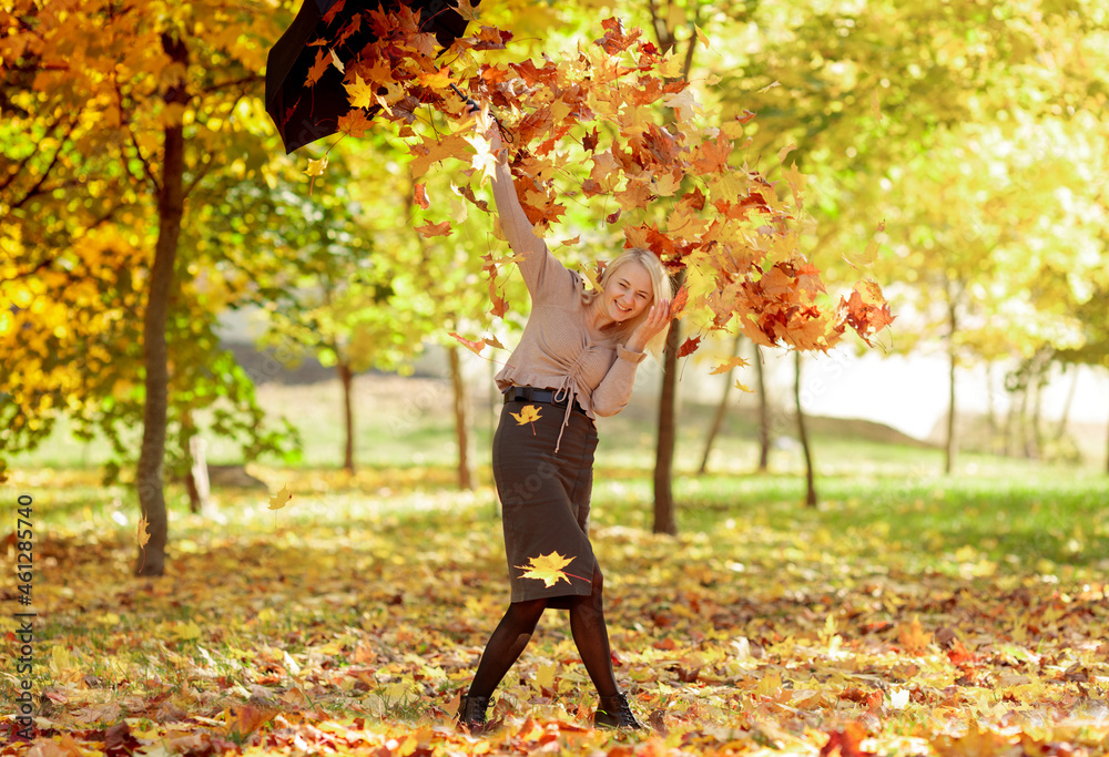 Young woman in the park sprinkles autumn leaves on herself from an umbrella Young woman in the park sprinkles autumn leaves on herself from an umbrella