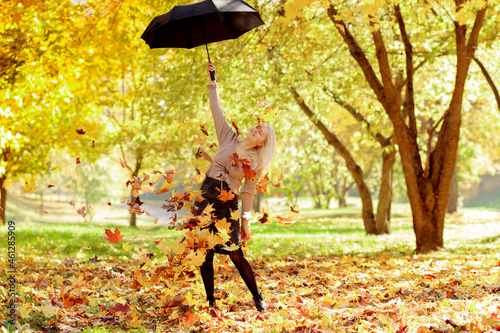 Young woman in the park sprinkles autumn leaves on herself from an umbrella